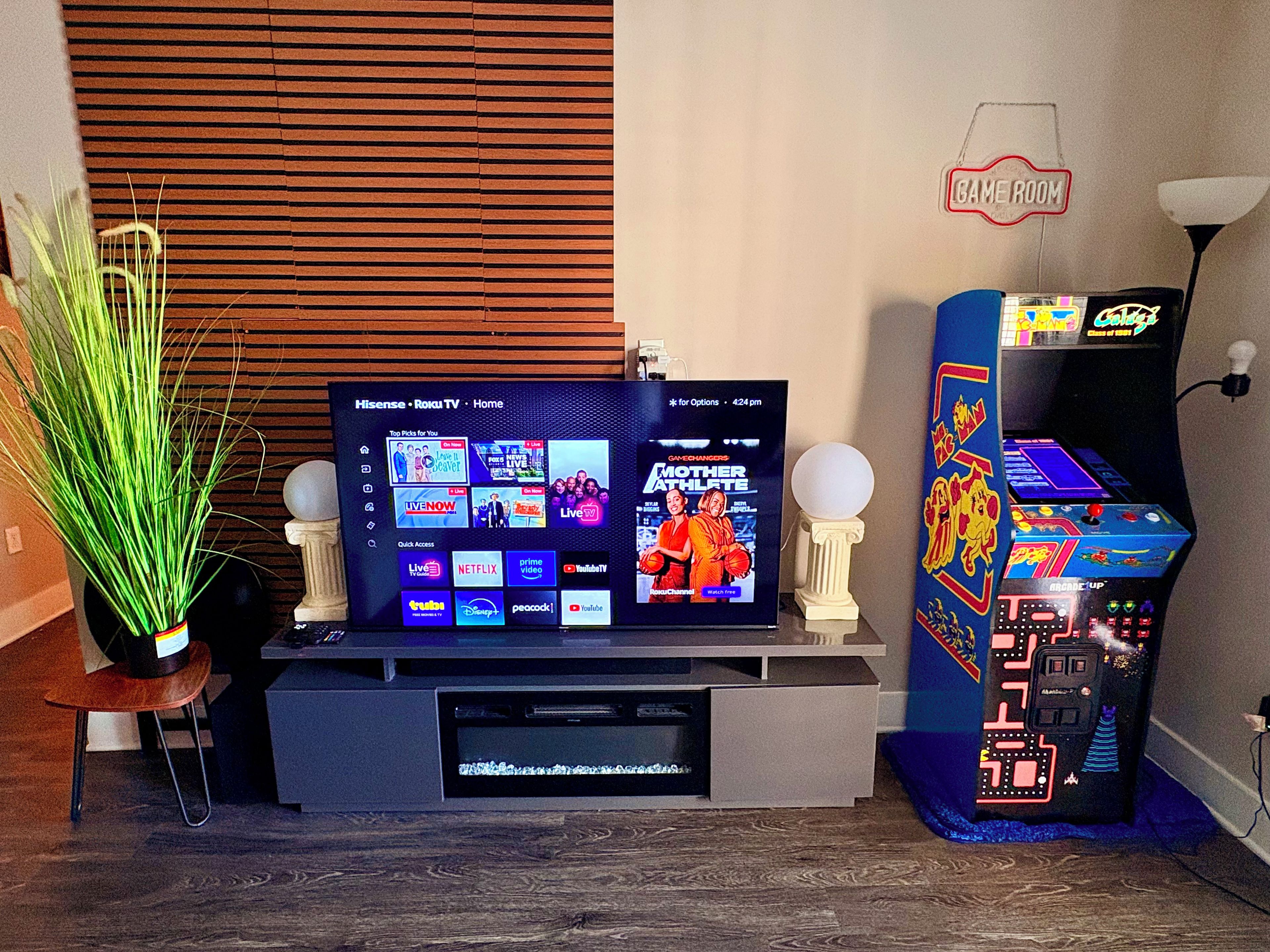 A television displaying a streaming service interface, a retro arcade machine, and a decorative sign.