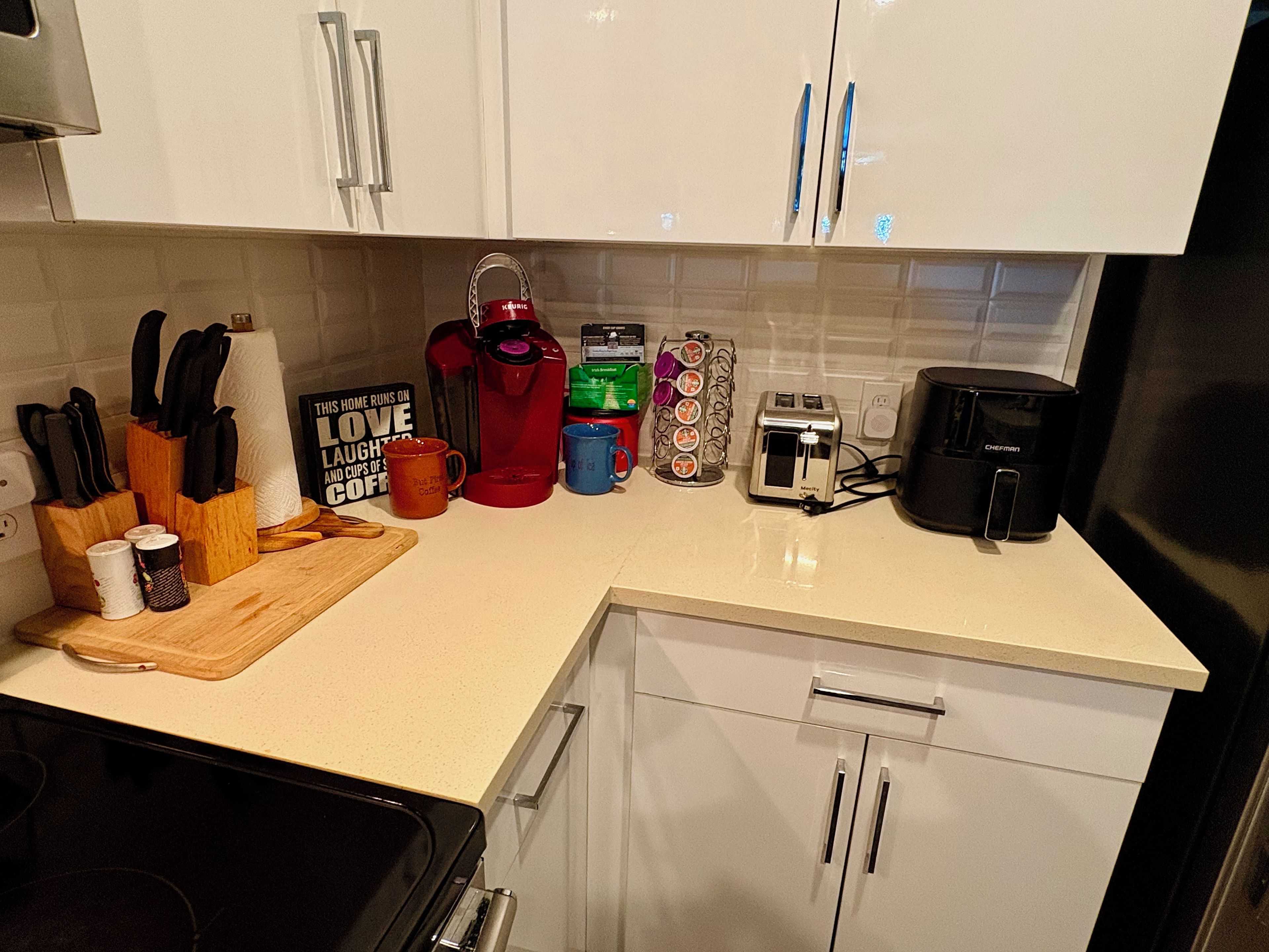 A kitchen with white cabinets, a toaster, a coffee maker, and various mugs and utensils on the counter.
