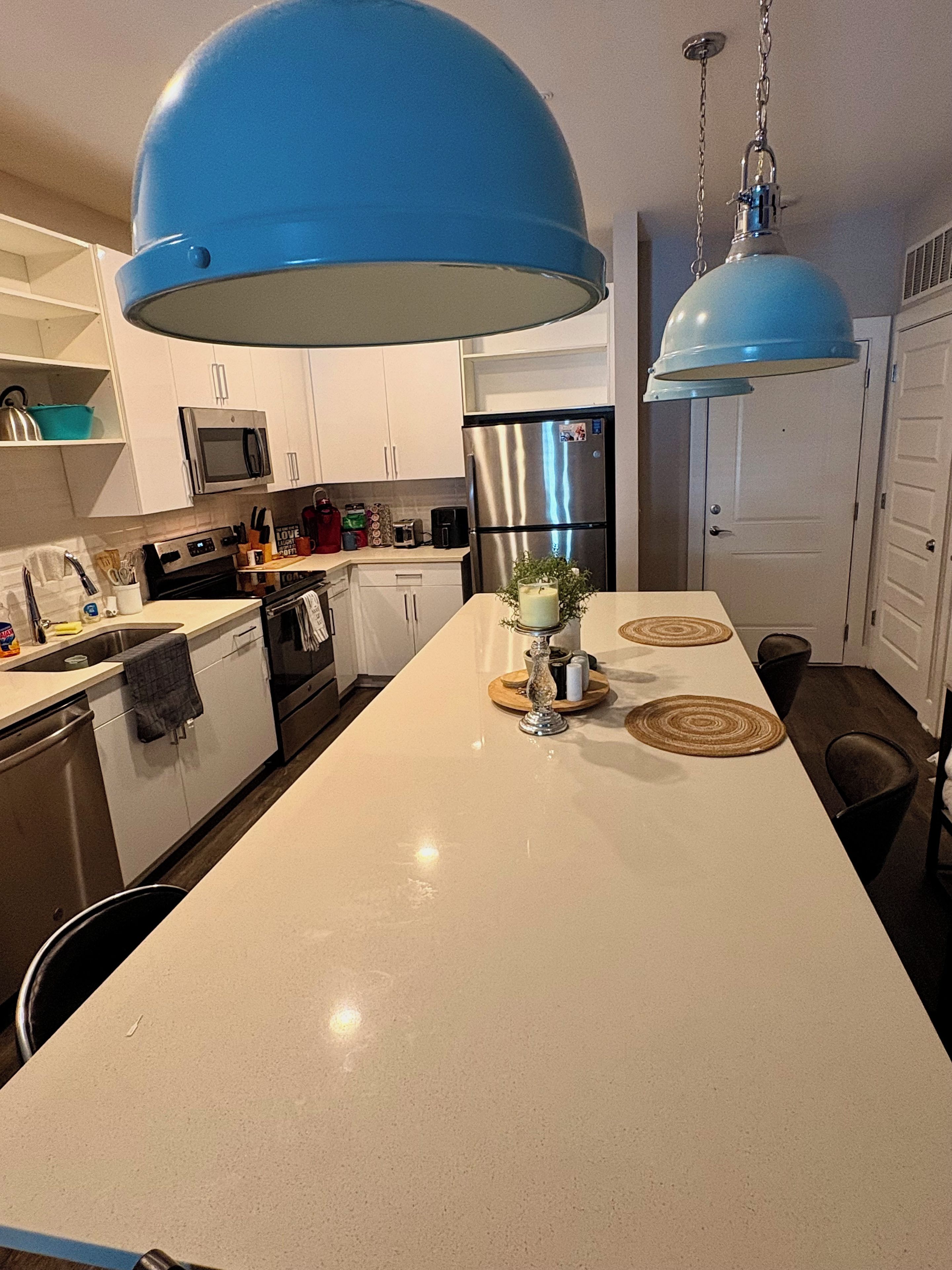 A modern kitchen with white cabinets, stainless steel appliances, and a central island with a blue pendant light.