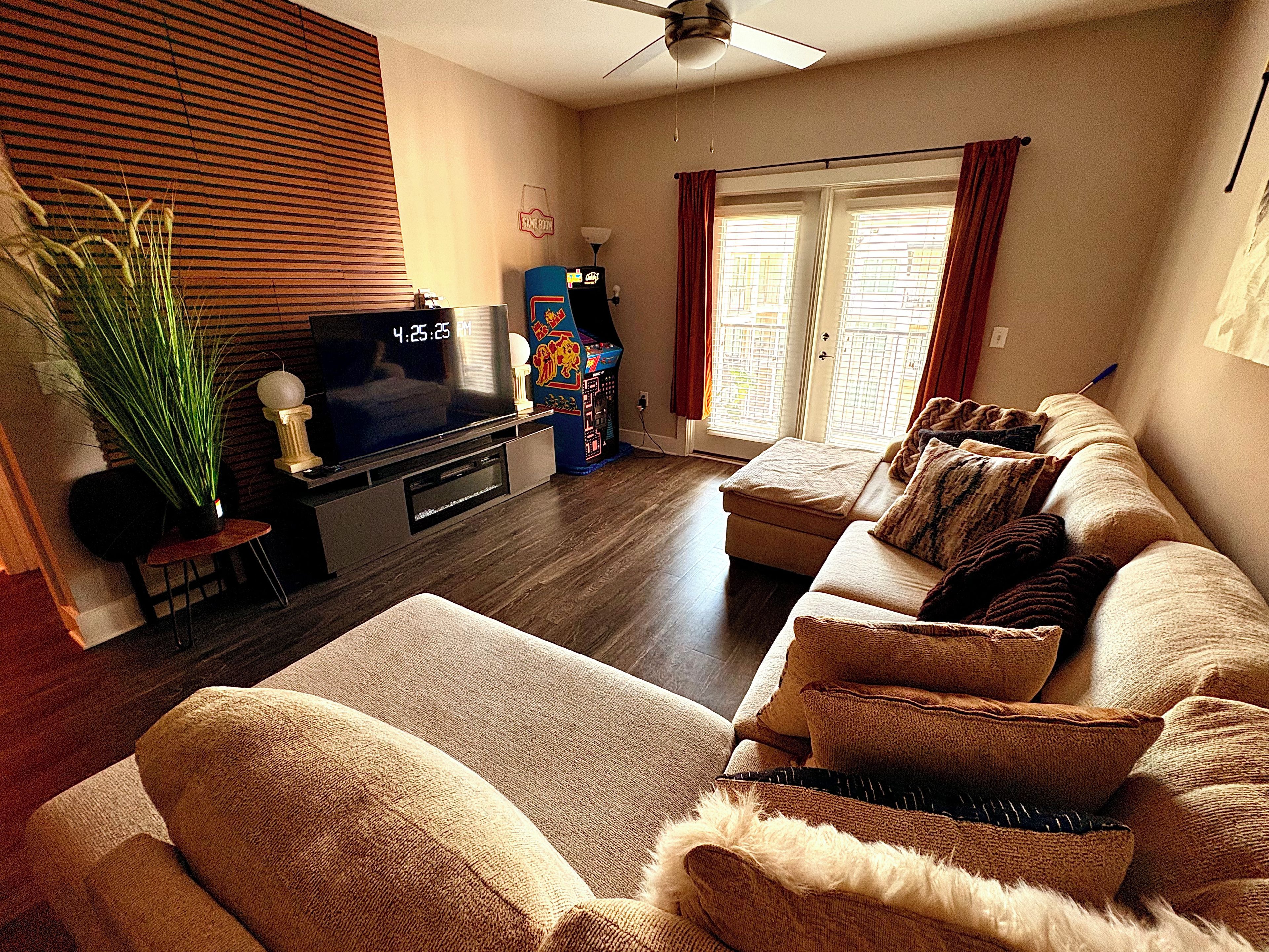 A living room with a flat-screen TV, a game machine, a sofa, and a potted plant.