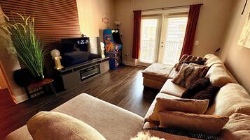 A living room with a flat-screen TV, a game machine, a sofa, and a potted plant.