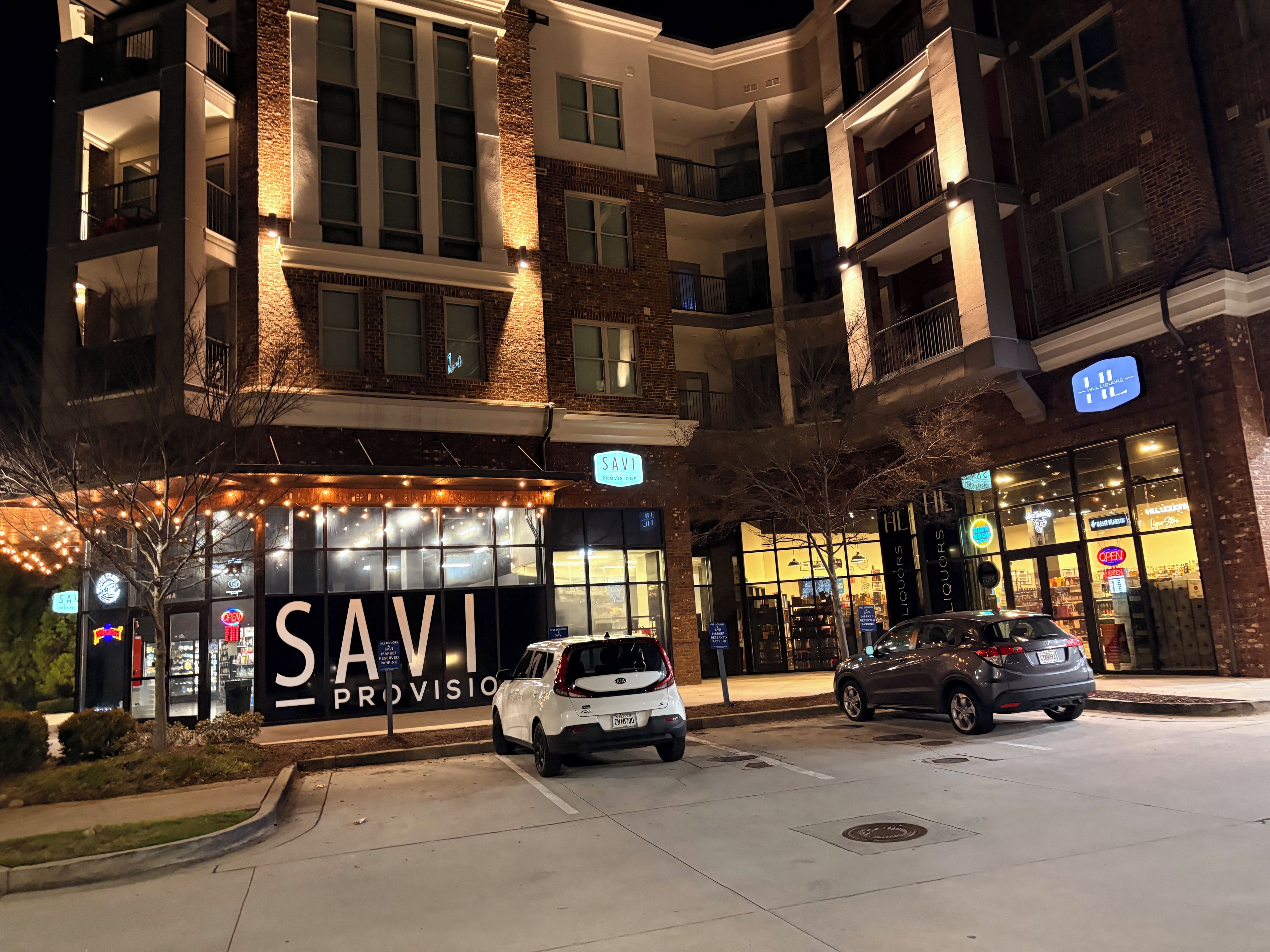 A multi-story building with a sign for 'SAVI PROVISIONS' and a parking area with two cars.