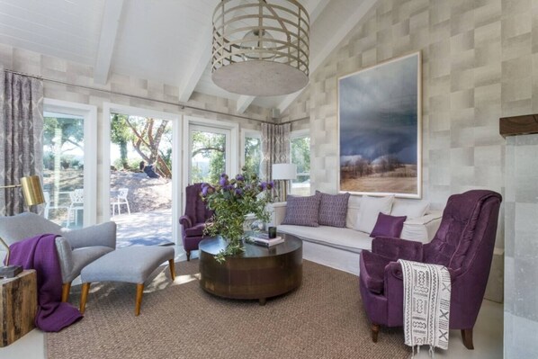Un salon spacieux au design moderne, comprenant un canapé, des fauteuils, une table basse et une grande fenêtre donnant sur l’extérieur.