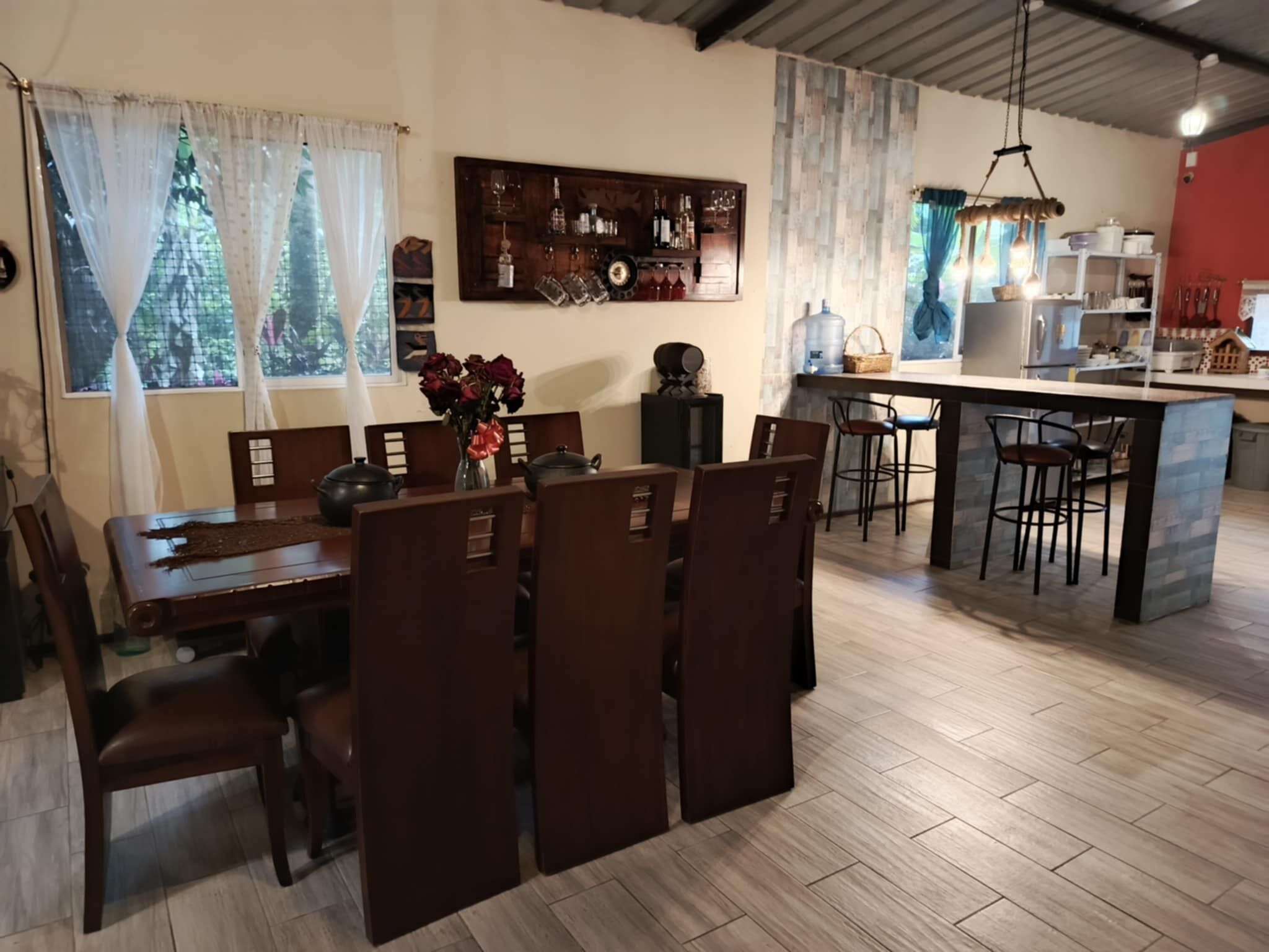 A dining area with a wooden table and chairs, a vase of flowers, and a bar area with shelves of bottles and glasses.