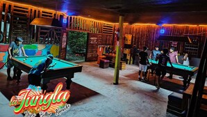 Una sala de billar con varias mesas de billar, paredes de madera y decoración temática de selva.