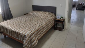 Une chambre dotée d’un grand lit, d’une table de chevet avec une lampe, et donnant sur un espace de vie attenant.