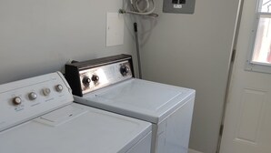 Une buanderie équipée de deux machines à laver et deux sèche-linge blancs, d’un chauffe-eau et d’une porte avec une fenêtre.