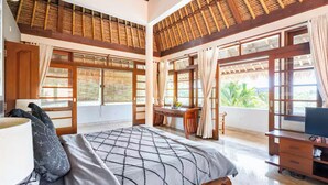 A bedroom with a bed, desk, and TV, large windows, and a balcony with a view.