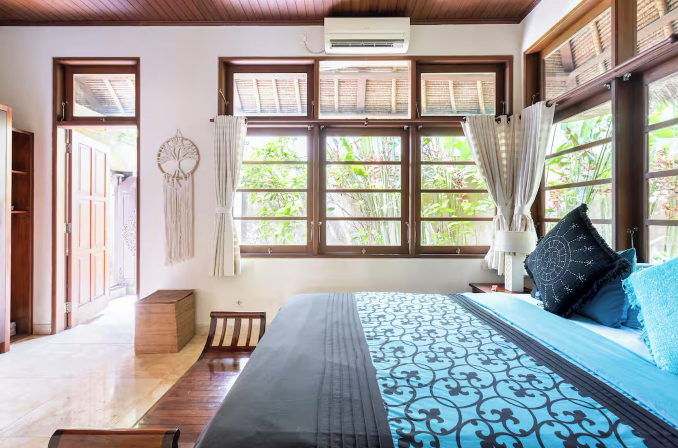 A bedroom with a large bed, multiple windows, and a view of greenery outside.