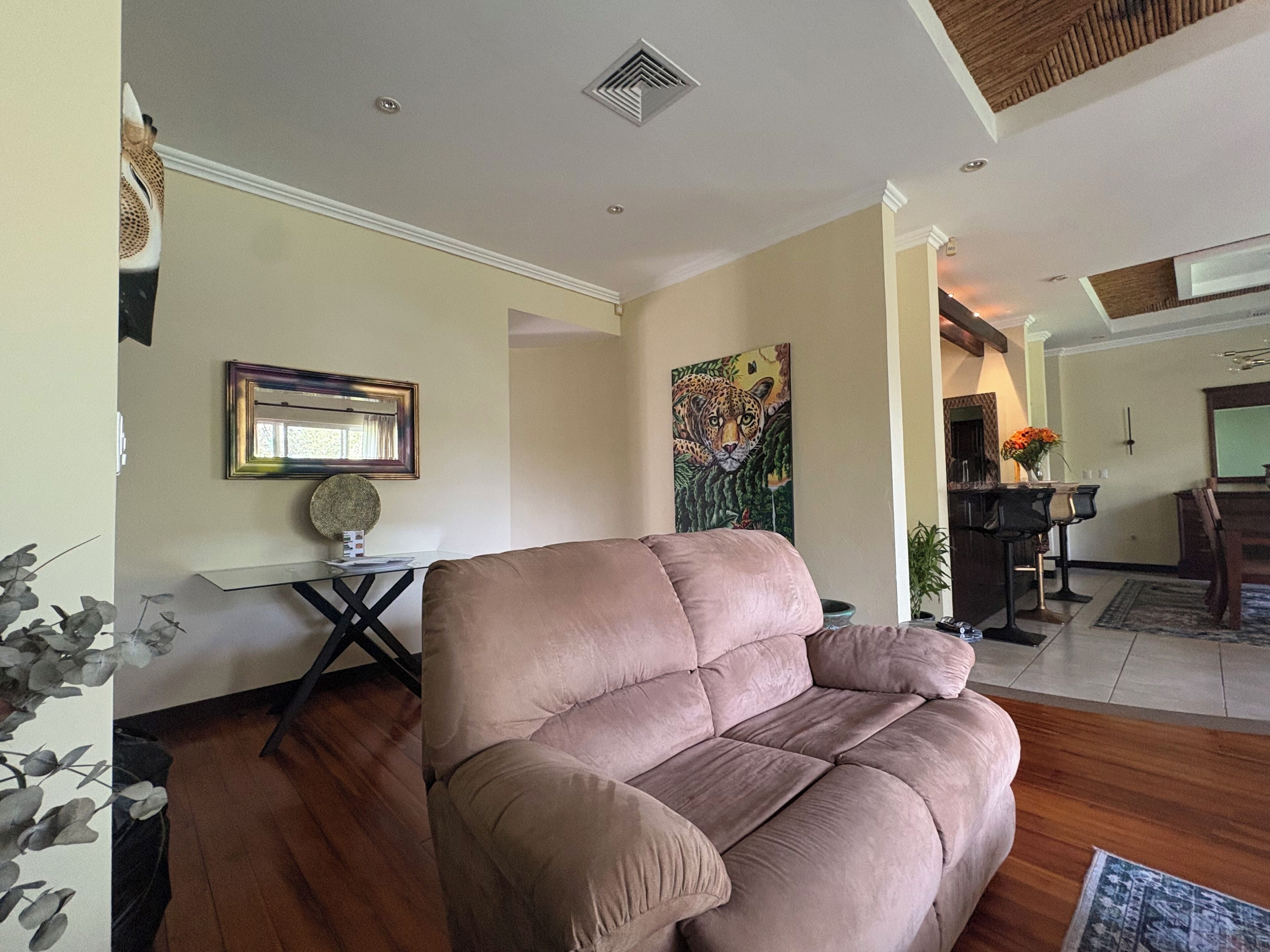 A living room with a large beige sofa, a dining area with a wooden table and chairs, and a painting of a leopard on the wall.