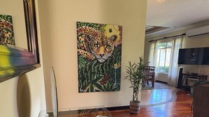Una sala de estar con piso de madera, un cuadro grande de un leopardo, un televisor de pantalla plana y un comedor con mesa y sillas.