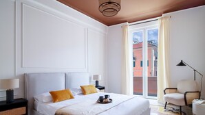 Quarto de hotel com uma cama grande, uma mesa de cabeceira, uma cadeira e uma janela com cortinas.