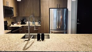 A modern kitchen with wooden cabinets, a stainless steel refrigerator, a microwave, and a coffee maker.