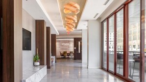 A modern hotel lobby with a marble reception desk, a seating area with chairs, and large windows offering views of the city.