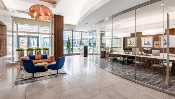 A modern lobby with a curved ceiling, glass walls, a seating area with blue chairs, and a large window offering a city view.