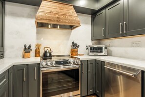 Una cocina con estufa, microondas y horno de acero inoxidable, armarios de madera y encimera blanca.