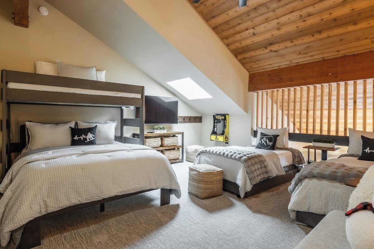A bedroom with two beds, a skylight, wooden beams, a television, and a small table with a plant.