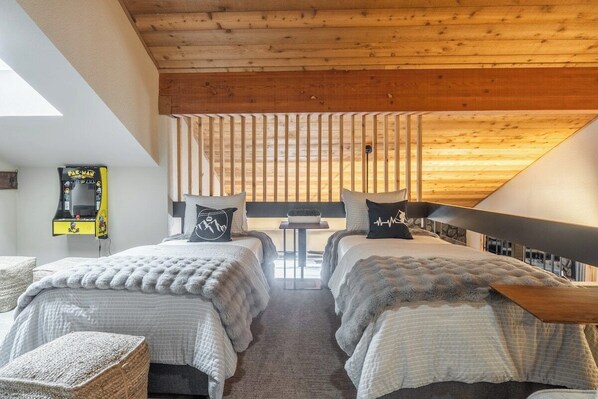 A bedroom with two beds, a small table, and a view of the outside.