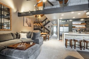 Un interior moderno con un sofá gris, una mesa de centro de madera y una escalera que sube a un nivel superior.