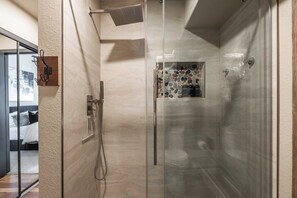 A modern bathroom with a glass-enclosed shower, a visible toilet, and a small window with a mosaic design.
