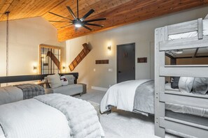 A room with bunk beds, a ceiling fan, a staircase, and wall-mounted lights.