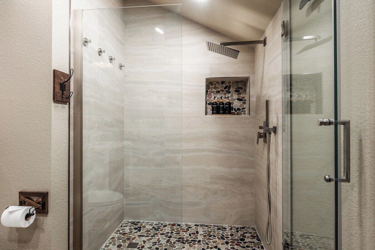 A glass-enclosed shower with a tiled floor, a towel dispenser, and a small shelf with toiletries.