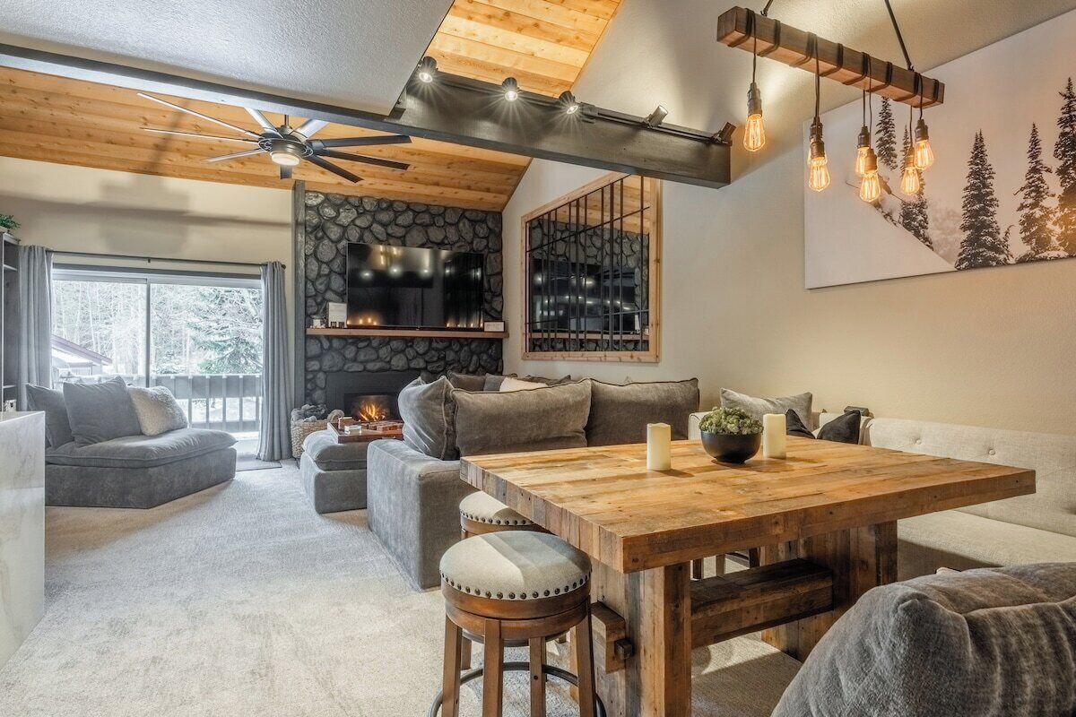 A cozy living room with a fireplace, a wooden ceiling, and a large window.