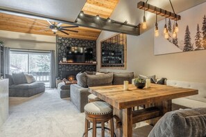 A cozy living room with a fireplace, a wooden ceiling, and a large window.