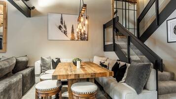 Um interior moderno com uma mesa de jantar de madeira, assentos acolchoados, uma escada e uma obra de arte emoldurada na parede.