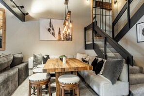 A modern interior with a wooden dining table, cushioned seating, a staircase, and a framed artwork on the wall.