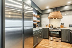 A modern kitchen with stainless steel appliances, dark cabinetry, and a wooden range hood.