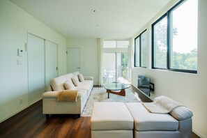 Uma sala de estar moderna com sofá, apoio para os pés, mesa de centro de vidro e televisão na parede.