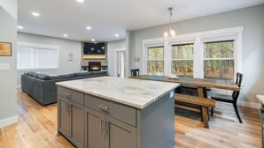 Une cuisine spacieuse dotée d’un grand îlot central, d’un coin repas avec une table en bois et d’une cheminée intégrée.
