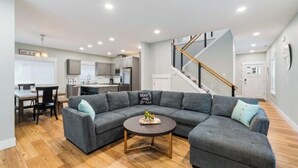 Un salon moderne avec un canapé d’angle, une table basse ronde et un escalier menant à l’étage supérieur.