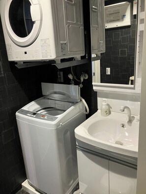 Ein kleines Badezimmer mit Waschmaschine, Waschbecken und Spiegel.