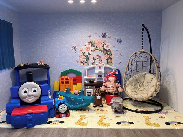 Ein Spielzimmer mit einem Thomas-Lokomotive-Spielzeug, einem blauen Spielzug, einem Spielhaus, einem Spielzeugauto, einem Spielzeugpferd und einer Modelleisenbahnstrecke.