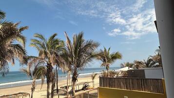 A wooden deck with a pool, overlooking a beach with palm trees and the ocean.