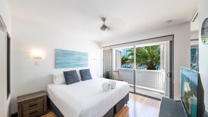 A bedroom with a bed, a nightstand, a painting, a ceiling fan, and a view of a pool through a sliding door.