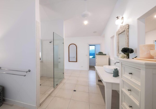 A modern bathroom with a glass shower enclosure, a white vanity with drawers, a large mirror, and a view to the outside.