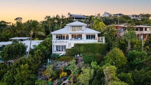 Una casa de dos pisos rodeada de abundante vegetación y otras edificaciones residenciales.