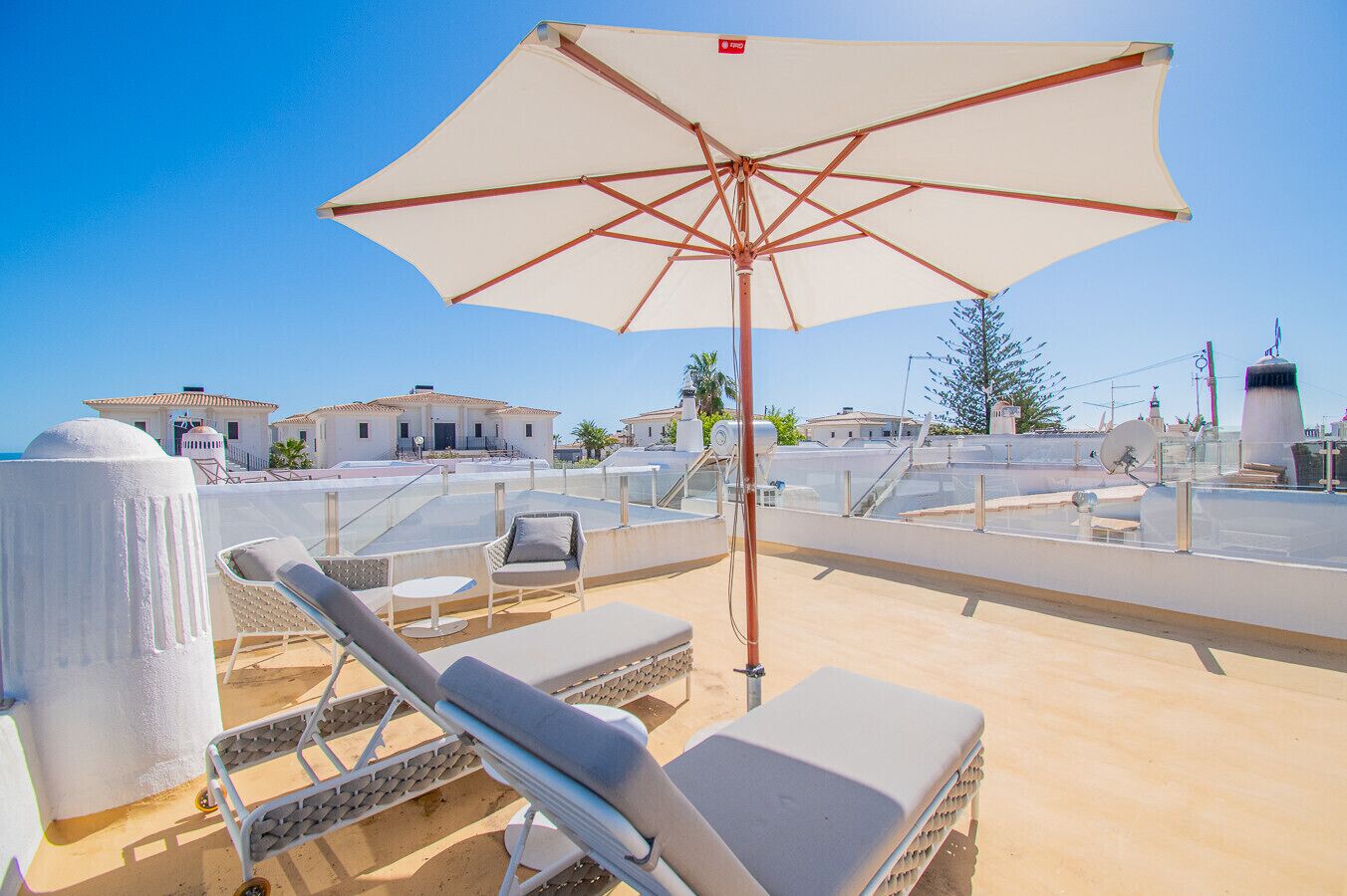 En tagterrasse med liggestole, en stor parasol og udsigt til bygninger i baggrunden.