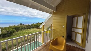 Uma varanda com vista para o oceano, piscina e uma cadeira amarela.