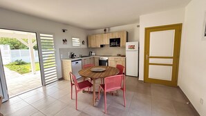 Cozinha compacta com área de jantar, apresentando uma mesa de madeira e cadeiras vermelhas, um refrigerador branco e um micro-ondas.