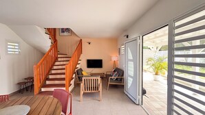 Sala de estar com escada de madeira, TV de tela plana, sofá e área de jantar com cadeiras.