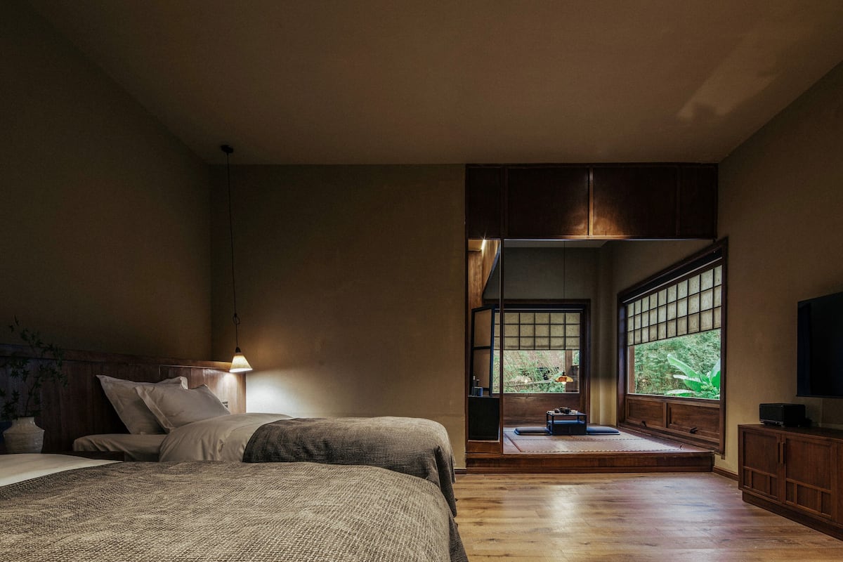 A bedroom with a bed, a TV, and a view of the outdoors through a window.