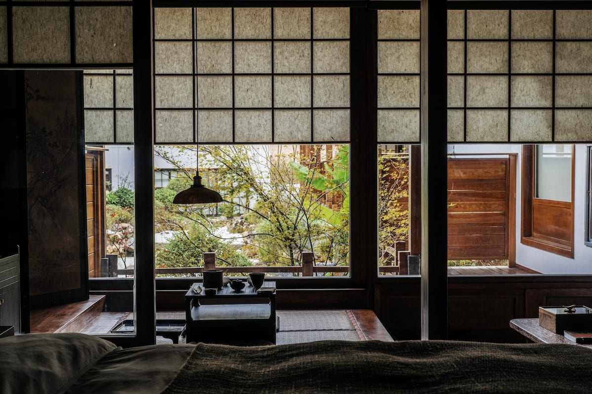 A traditional Japanese-style room with tatami flooring, a low table with a tea set, and a view of a garden through shoji screens.