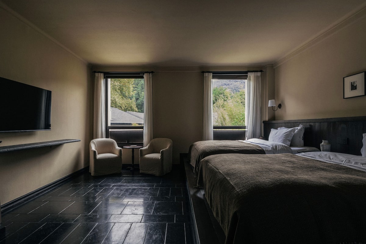 A hotel room with two beds, a TV, a small table, and two chairs.