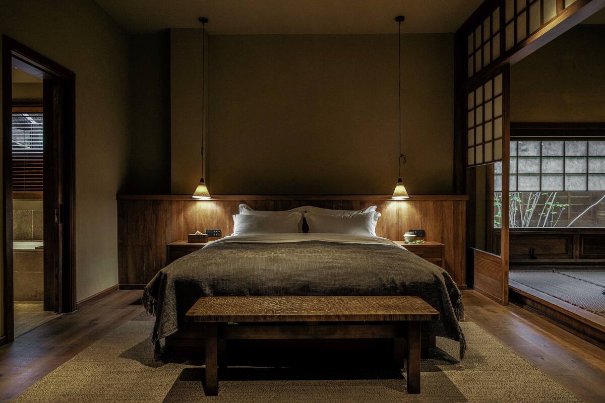 A traditional Japanese-style bedroom with a wooden bed, two bedside tables, and a view of a garden through a sliding door.