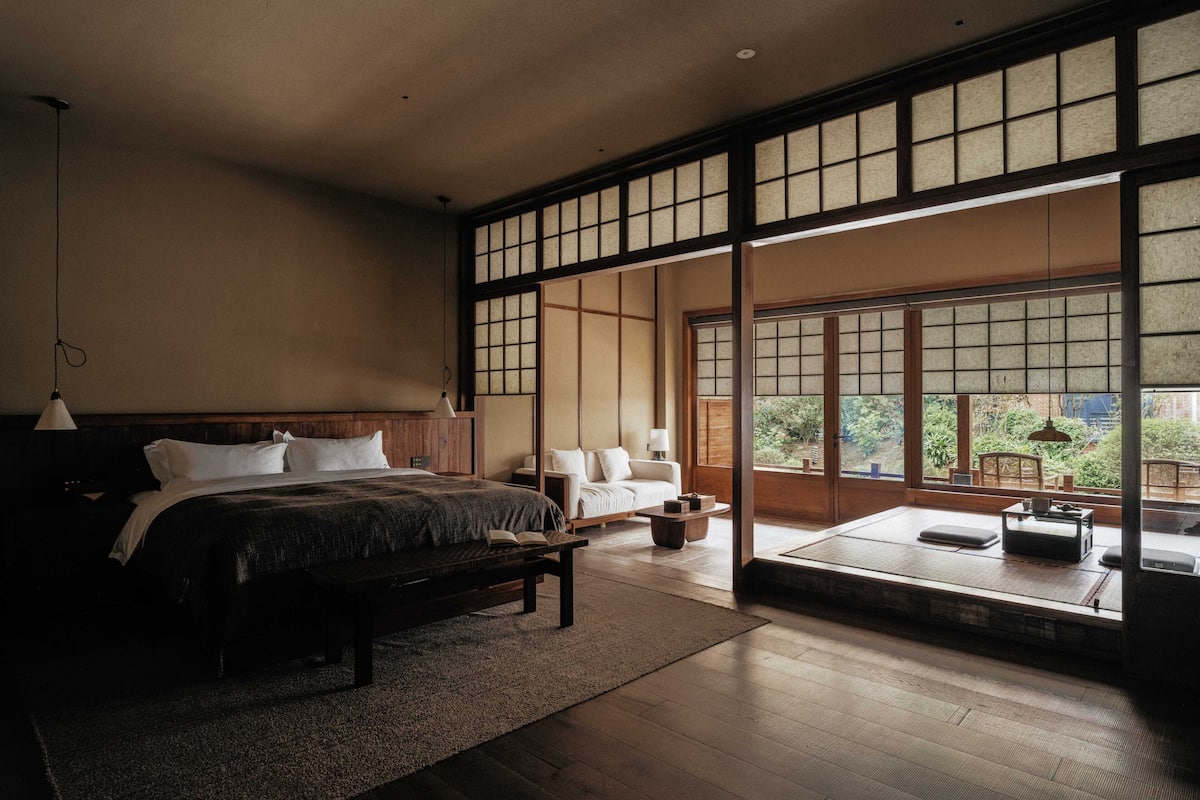 A traditional Japanese-style bedroom with tatami flooring, a large sliding door leading to a balcony, and a bed with a wooden headboard.