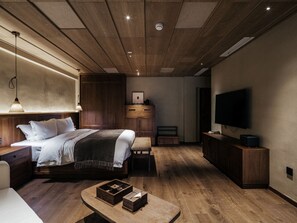 Quarto moderno com teto de madeira, cama com roupa de cama branca, mesa de cabeceira, televisão e armário de madeira.